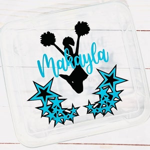 May include: A clear plastic container with a black silhouette of a cheerleader with pom-poms and the name Makayla written in blue cursive. The container is decorated with blue and black stars.