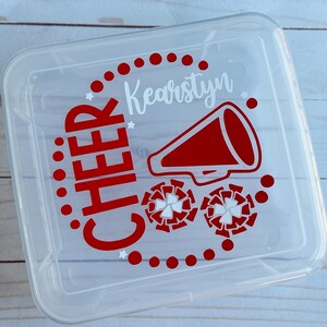 Puede incluir: Contenedor de almacenamiento de pl&aacute;stico transparente con un dise&ntilde;o rojo y blanco. El dise&ntilde;o incluye las palabras "CHEER" y "Kearstyn" junto con un meg&aacute;fono y pompones de animadora.