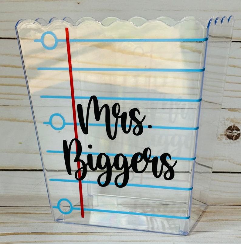 Puede incluir: Contenedor de pl&aacute;stico transparente con un dise&ntilde;o de rayas azules y blancas. El contenedor tiene una l&iacute;nea roja en el lateral y el texto "Mrs. Biggers" en negro.