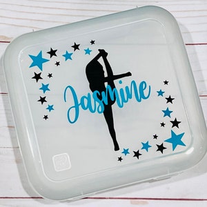 May include: A white plastic container with a clear lid. The lid has a black silhouette of a gymnast with the name "Jasmine" written in blue cursive. The design is surrounded by black and blue stars.