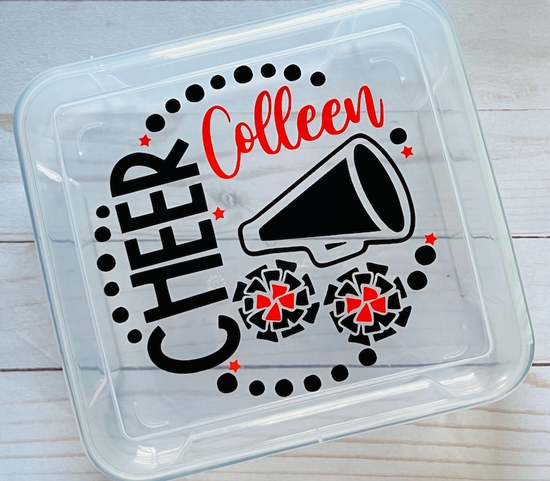 Puede incluir: Contenedor de almacenamiento de pl&aacute;stico transparente con un dise&ntilde;o en negro y rojo. El dise&ntilde;o incluye las palabras "CHEER Colleen" y un meg&aacute;fono negro con estrellas rojas. Tambi&eacute;n hay dos pompones rojos y negros.
