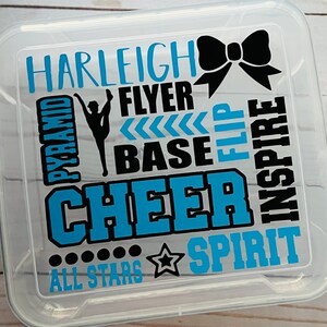 May include: Clear plastic storage box with a blue and black design. The design includes the words "Harleigh Cheer", "Pyramid", "Flyer", "Base", "Flip", "Inspire", "Spirit", and "All Stars".