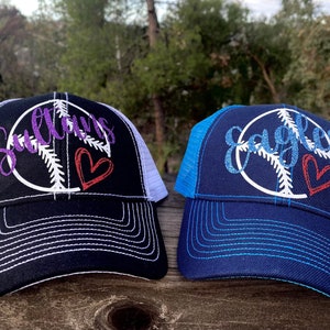 May include: Two black baseball caps with white mesh back panels. The front of each cap features a white peace sign with a baseball inside. The word "Sultans" is embroidered in purple on one cap and "Eagles" is embroidered in blue on the other cap. Both caps have a red heart embroidered on the peace sign.