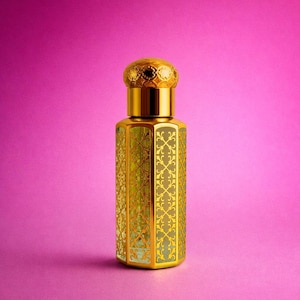 Puede incluir: Frasco de perfume dorado con un diseño ornamental. El frasco tiene un tapón decorativo y un exterior estampado. El fondo es de color rosa liso.
