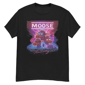 Op de afbeelding: Zwart T-shirt met een afbeelding van drie cartoon elanden met zonnebrillen, met het woord "MOOSE" erboven. Onder de elanden staat de tekst "SIMULATION Theory". Het ontwerp heeft een retro, neon esthetiek.