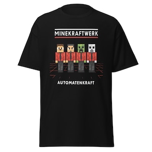 May include: Black t-shirt with a pixelated graphic of four figures in red shirts and grey trousers. The text "MINEKRAFTWERK" is above the figures, and "AUTOMATENKRAFT" is below. A red and orange grid design is behind the figures.
