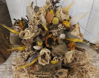 Può includere: Un bouquet di fiori secchi con rose color crema, accenti gialli e piume. La composizione è presentata in un contenitore rustico con testo a tema caffè, su un letto di paglia. Un elemento decorativo naturale e terroso.