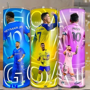 Könnte beinhalten: Drei Edelstahlbecher mit den Fußballspielern Neymar Jr., Cristiano Ronaldo und Lionel Messi. Jeder Becher hat eine andere Hintergrundfarbe: blau, gelb und rosa. Das Wort "GOAL" ist auf jedem Becher in fetter, weißer Schrift gedruckt.