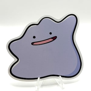 Op de afbeelding: Een witte keramische mok met een zwarte handgreep en de tekst "But First, Coffee" in een vetgedrukte, zwarte letter. De mok staat op een houten oppervlak. De mok is ongeveer 10 cm hoog.