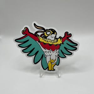 Könnte beinhalten: Ein farbenfroher Aufkleber mit einer cartoonartigen, vogelähnlichen Kreatur mit ausgebreiteten Flügeln. Das Design umfasst die Farben Rot, Türkis, Gelb und Weiß mit schwarzen Umrissen. Der Aufkleber wird auf einem transparenten Ständer vor weißem Hintergrund präsentiert.