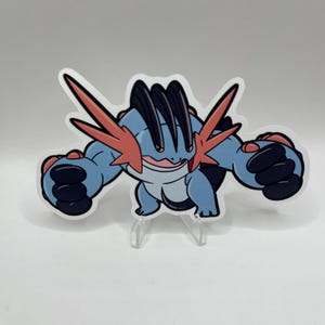 May include: A sticker featuring a cartoon-style Swampert character. The character is primarily blue with black and red accents. It has a wide stance and is displayed on a clear stand against a white background.