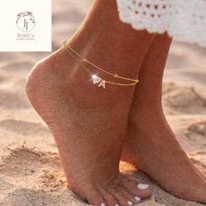 May include: A gold-coloured double-layered anklet featuring a heart-shaped charm and the letter "A". The anklet is decorated with small, round embellishments. The image also shows the logo "Jenny's Jewellery".