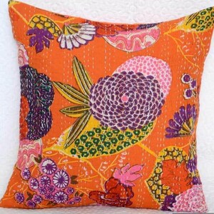 May include: Square orange pillow with a floral design. The pillow features a vibrant pattern of purple, pink, yellow, and green flowers and leaves. The pillow has a stitched texture and a solid orange background.