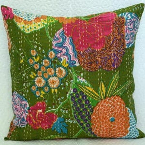 May include: A square decorative pillow with a green background and colorful floral patchwork design. The patchwork includes orange, pink, blue, and yellow floral and abstract patterns. White stitching outlines the patchwork.