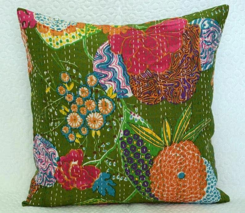 May include: A square decorative pillow with a green background and colorful floral patchwork design. The patchwork includes orange, pink, blue, and yellow floral and abstract patterns. White stitching outlines the patchwork.