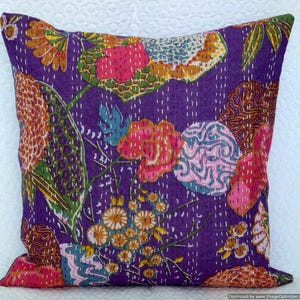May include: Square decorative pillow with a vibrant floral pattern on a purple background. The design features pink, orange, and blue flowers with white stitching. This pillow adds a pop of color to any room.