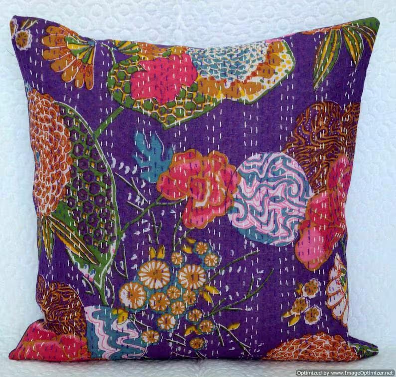 May include: Square decorative pillow with a vibrant floral pattern on a purple background. The design features pink, orange, and blue flowers with white stitching. This pillow adds a pop of color to any room.