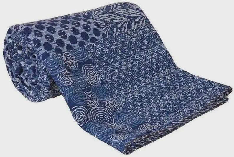 May include: Rolled-up blue and white patterned quilt. The quilt features a variety of designs, including circles and floral patterns. The color scheme is primarily indigo and white, creating a visually appealing contrast. The quilt is made of a soft, likely cotton material.