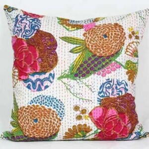 May include: Square throw pillow with a white background and a colorful floral pattern. The design features large flowers in shades of pink, brown, and orange, with green leaves and blue accents. The pillow has a stitched texture.