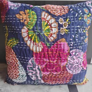 May include: Square decorative pillow with a navy blue background and a floral pattern in shades of pink, yellow, green, and white. The pillow has a quilted design with white stitching.