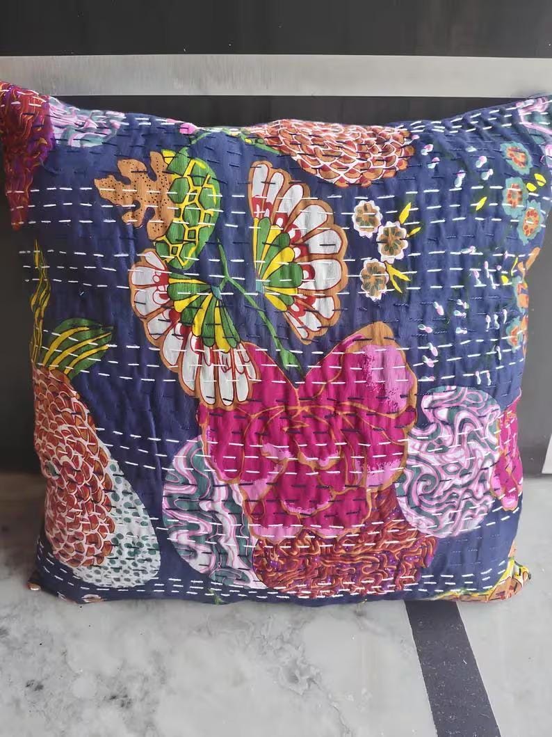 May include: Square decorative pillow with a navy blue background and a floral pattern in shades of pink, yellow, green, and white. The pillow has a quilted design with white stitching.