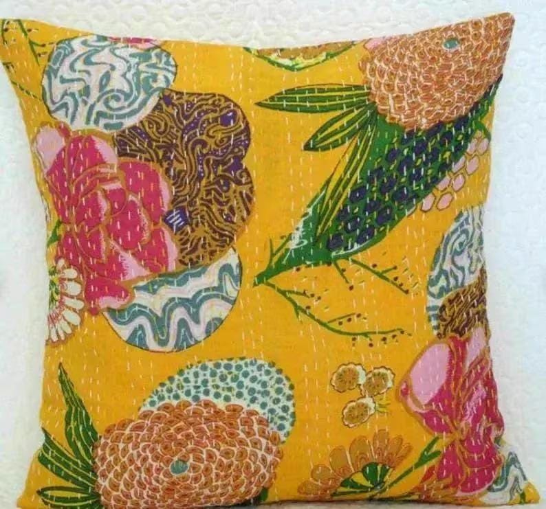 May include: A square decorative pillow with a bright yellow background. The pillow features a floral pattern with pink, brown, green, and blue accents. The design is stitched onto the fabric.