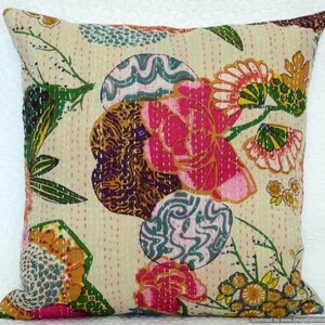 May include: Square decorative pillow with a cream-colored background and colorful floral patterns. The design features large pink flowers, green leaves, and abstract shapes in blue, brown, and yellow. The pillow has a stitched texture.