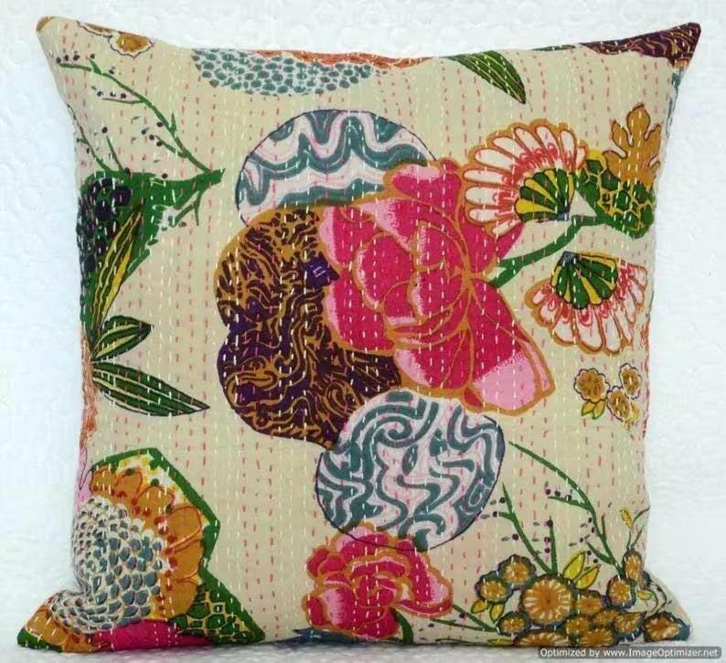 May include: Square decorative pillow with a cream-colored background and colorful floral patterns. The design features large pink flowers, green leaves, and abstract shapes in blue, brown, and yellow. The pillow has a stitched texture.
