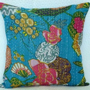 May include: Square throw pillow with a vibrant floral pattern. The pillow features a turquoise background with large pink and yellow flowers, green leaves, and white stitching. The design is reminiscent of a vintage textile.