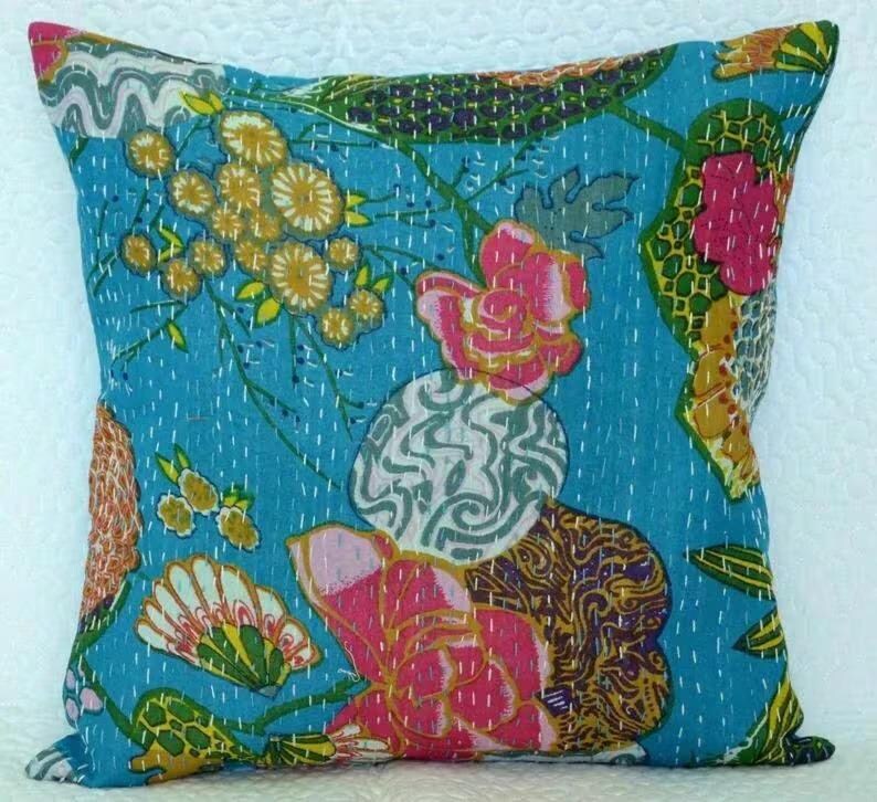 May include: Square throw pillow with a vibrant floral pattern. The pillow features a turquoise background with large pink and yellow flowers, green leaves, and white stitching. The design is reminiscent of a vintage textile.
