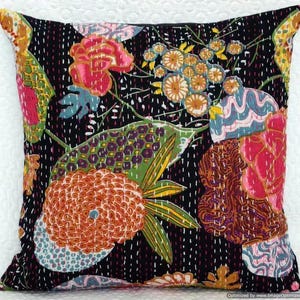 May include: Square decorative pillow with a black background and a colorful floral pattern. The design features large flowers in shades of pink, orange, and yellow, with green leaves and blue accents. The pillow is embellished with white stitching.