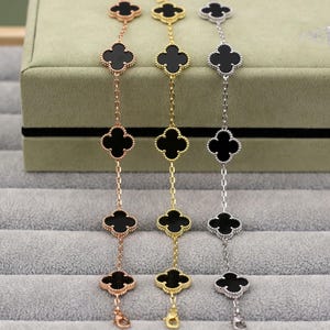 Puede incluir: Tres pulseras con abalorios en forma de trébol y centros negros. Las pulseras son en tonos oro rosa, oro y plata. Cada pulsera tiene una cadena con múltiples abalorios de trébol.