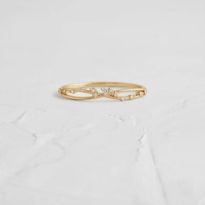 Op de afbeelding: Een delicate gouden ring met een uniek, verweven ontwerp. De ring is voorzien van kleine, sprankelende diamanten langs de band, wat een vleugje elegantie toevoegt. De ring is geplaatst tegen een witte achtergrond.