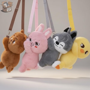 Puede incluir: Cuatro bolsos cruzados de peluche en marrón, rosa, gris y amarillo. Cada bolso presenta un diseño de animal diferente: un oso, un conejito, un lobo y un pato. Los bolsos tienen correas de colores a juego y herrajes plateados.