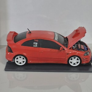 Può includere: Un modellino di auto rosso con ruote bianche e spoiler posteriore. Il cofano è aperto e mostra i dettagli del motore. Sul finestrino laterale è presente la scritta "SPEED HUNTERS" e sul finestrino posteriore è stampato il numero "305".