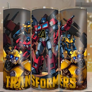 Op de afbeelding: Een roestvrijstalen beker met een levendig ontwerp van Transformers-personages, waaronder Optimus Prime en Bumblebee. Het woord "TRANSFORMERS" staat in grote, gele letters onderaan. De beker heeft een rietje en een deksel.