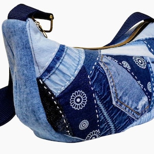 Puede incluir: Bolso bandolera de patchwork de mezclilla con una correa ajustable azul marino. El bolso presenta varios tonos de mezclilla azul, con costuras blancas y un estampado floral en un parche azul oscuro. Tiene una cremallera y herrajes dorados.