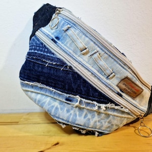 Puede incluir: Riñonera de mezclilla con diseño patchwork. La bolsa cuenta con cierre de cremallera, una pequeña etiqueta que dice "SPECIAL EDITION FOR YOU" y una correa negra. La mezclilla es una mezcla de lavados azul claro y oscuro.