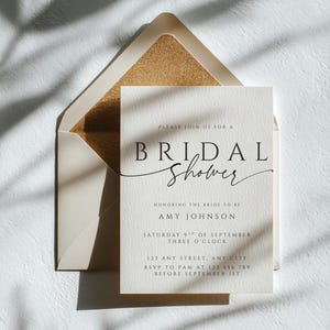Peut inclure: Une invitation à une fête prénuptiale avec une carte et une enveloppe crème. L'invitation présente les mots "BRIDAL Shower" dans une police élégante, ainsi que le nom de la mariée, la date, l'heure et les informations RSVP. L'enveloppe a un intérieur doré scintillant.