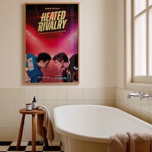 May include: A framed poster for "Heated Rivalry" hangs above a white bathtub in a bathroom. The poster features two football players facing each other. A small wooden stool with a towel and toiletries sits nearby. The bathroom has white tile and a checkered floor.