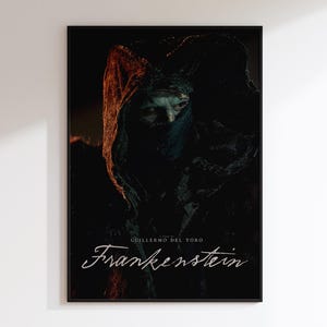 May include: A framed film poster for Guillermo del Toro's "Frankenstein." The poster displays a dark, dramatic image of a figure in a hooded cloak with a partially obscured face. The title "Frankenstein" is written in elegant script.
