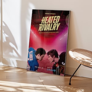 May include: A framed poster for "Heated Rivalry" leans against a wall. The poster features two young men facing each other, with the title in large, bold letters. The background is a stadium scene with red and purple hues. The text "Crave Original" is at the top.
