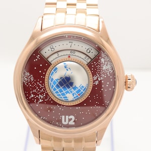 May include: A rose gold wristwatch with a burgundy face featuring a world map design and the text "U2." The watch has a gold-colored band and a round face with a unique time display.