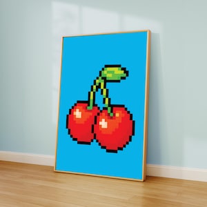 May include: A framed print showing a pixelated image of two red cherries with green stems and leaves on a vibrant blue backdrop. The artwork has a retro video game style and is displayed in a room with a wooden floor.