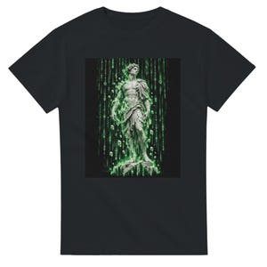 Könnte beinhalten: Ein schwarzes T-Shirt mit einem zentralen Grafikdruck einer klassischen Marmorstatue auf einem Steinsockel, umgeben von vertikalen Strömen aus leuchtend grünem digitalen Binärcode und schwebenden geometrischen Würfeln vor dunklem Hintergrund.