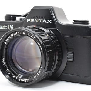 Puede incluir: Una taza de cerámica blanca con un asa negra y el texto "But First, Coffee" en negro, con una fuente de estilo manuscrito. La taza está sobre una superficie blanca.