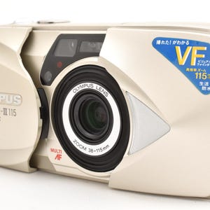 May include: A champagne-coloured Olympus Mju-II 115 VF film camera with a sliding lens cover. The front features a black lens barrel labelled 38-115mm, a Multi AF indicator, and a blue sticker with Japanese text and the letters VF 115.