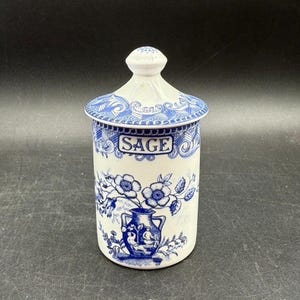 以下が含まれることがあります： 「SAGE」と書かれた、白と青のセラミックジャー。ジャーには青色の花柄と花瓶のデザインが施されています。蓋には装飾的なつまみが付いています。円筒形のジャーは、ハーブやスパイスの保管に使用される可能性があります。