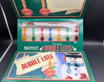 Può includere: Una scatola di Midwest of Cannon Falls Christmas Bubble Lites con sette luci a bolle multicolori dietro una finestra in plastica trasparente. La confezione verde riporta il testo Christmas Bubble Lites e un pupazzo di neve.