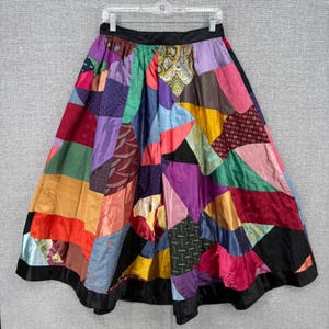 Pode incluir: Uma saia patchwork colorida com cós e bainha pretos. A saia é feita de várias peças de tecido em tons de vermelho, laranja, amarelo, verde, azul, roxo e rosa. A saia está pendurada em um cabide.